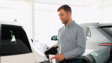 Elektrikli araca kablo bağlayan ve araba galerisinde pilleri şarj eden bir adam..