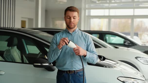 車のブロガーまたはセールスマンは新しい電気自動車の充電ケーブルを示します — ストック動画