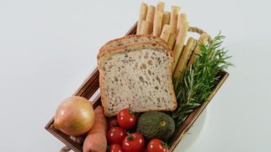 Taze sebzeli ahşap sepet, peynirli ekmek çubukları ve taze ekmek beyaz üzerinde döner..