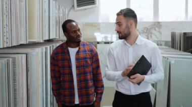 Afro-Amerikalı bir adam ev banyosu ya da mutfağı için seramik fayanslar seçiyor ve erkek satıcı doğru kararı vermesine yardımcı oluyor.