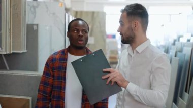 Afro-Amerikalı bir adam ev banyosu ya da mutfağı için seramik fayanslar seçiyor ve erkek satıcı doğru kararı vermesine yardımcı oluyor.