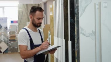 Erkek işçi, satış müdürü inşaat mağazasında döşeme envanteri çıkarıyor.