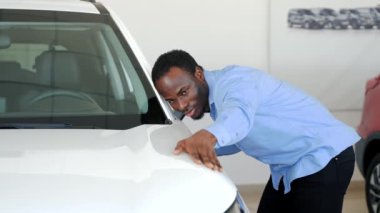 Yakışıklı siyah adam yeni arabasını okşuyor ve gülümsüyor.
