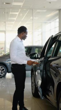 Gülümseyen, dost canlısı araba satıcısı araba kuaföründe açık kapı ve yeni araba gösteriyor.