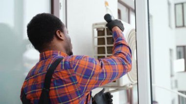 Afrika kökenli Amerikalı teknisyen dışarıdaki duvara klima yerleştiriyor. Hvac hizmetleri.