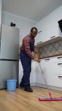 Komik, neşeli profesyonel temizlikçi yerleri silerken paspasla dans ediyor.