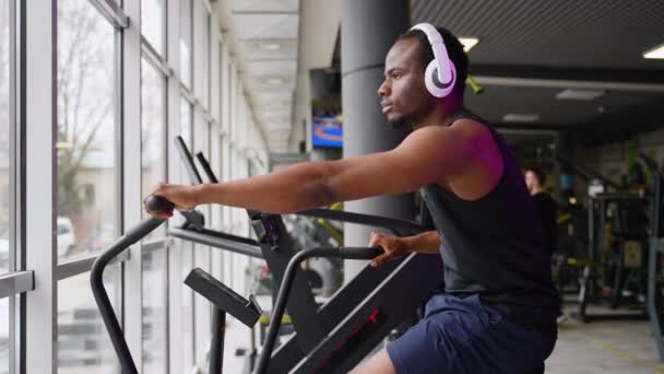 Afroamerikansk Man Med Hörlurar Gör Konditionsträning Stationär Luftcykel Maskin Med — Stockvideo