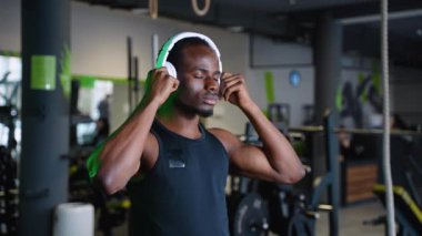 Spor giyim bölümünde spor giyim kuşamında genç ve yakışıklı Afro-Amerikan bir adam. Akıllı telefonunu kullanıyor ve spor salonunda antrenman yaparken müzik dinliyor. Eğitimi için en iyi şarkı.