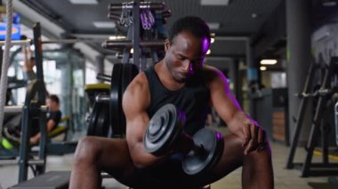 Afrikalı Amerikalı adam spor salonunda dambılla çalışıyor..