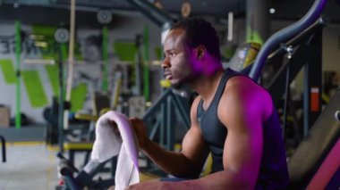 Spor kıyafetli genç bir zenci spor salonunda havlusuyla terliyor. Terli ve yorgun..