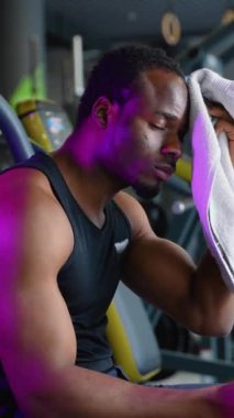 Spor kıyafetli genç adam spor salonunda havlusuyla terliyor. Terli ve yorgun.