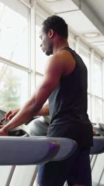 Formda bir adam spor salonunda çalışan bir makine üzerinde egzersiz yapıyor.