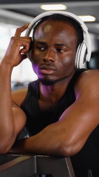 スポーツウェアのアフリカ系アメリカ人男性がジムでトレーニング中に音楽を聴く — ストック動画