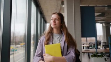 Üniversitede kitap ve çantayla dolaşan mutlu genç kız.