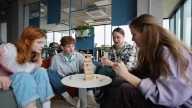 Bir grup mutlu genç arkadaş, tahta dikdörtgen bloklardan yapılmış bir masa oyunu oynuyorlar, kuleden parçalar çıkarıyorlar..