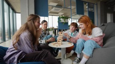 Genç mutlu insanlar kafede Jenga oynuyor, bir kız kuleden bir tahta bloğu kaldırıyor ve diğerleri izliyor..