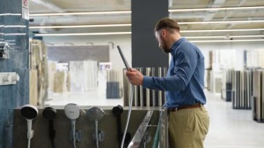 Bir adam elit bir tesisat dükkanında çeşme seçer. Alıcı satın almadan önce musluğu kontrol eder