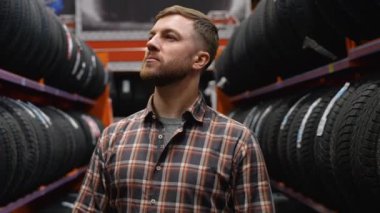 Lastik mağazasında yürüyen ve araba için yeni bir lastik seçen bir adam..