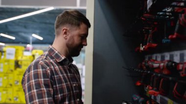 Hırdavatçıdaki bir adam yeni bir tornavida seçiyor. Yanında da tamirat için kullanılan elektrikli aletler var.