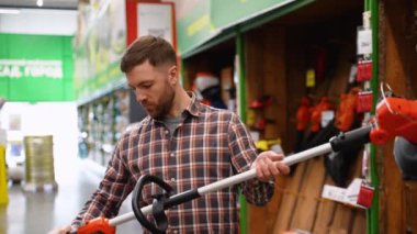 Bir adam bahçe malzemeleri dükkanında çim biçmek için elektrikli budama makinesi seçiyor..