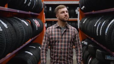 Lastik mağazasında yürüyen ve araba için yeni bir lastik seçen bir adam..