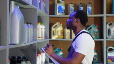 Depoda Afro-Amerikalı satıcı araba parçalarını kontrol ediyor ve not alıyor.