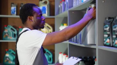 Depoda Afro-Amerikalı satıcı araba parçalarını kontrol ediyor ve not alıyor.