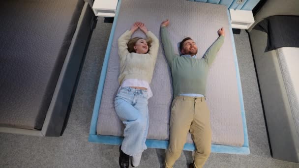 家具店でベッドを選択する陽気な若いカップル — ストック動画