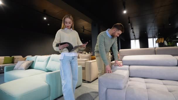 若いカップルは高級家具店のカタログのソファーを選びます — ストック動画