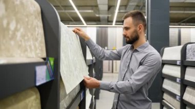 Ev eşyaları mağazasında tasarımcı duvar kâğıdı örnekleri arayan bir adam..