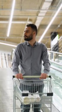 Hırdavatçıda yürüyen merdivende alışveriş arabası olan bir adam.