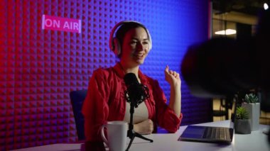 Kanal için vlog kaydetmek için mikrofon ve kulaklık kullanan bir kadın video kaydedici. Sosyal medya podcast 'i için modern ekipmanlarla video çeken pozitif kadın. Stüdyoda blogger kaydı