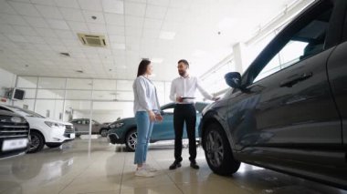 Güzel genç bayan galeride bir araba seçerken yakışıklı sakallı satış müdürüyle konuşuyor. Galeride arabaları kadınlara gösteren bir araba satıcısı.