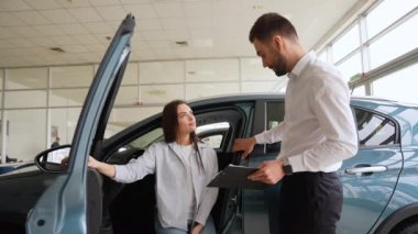 Güzel genç bayan galeride bir araba seçerken yakışıklı sakallı satış müdürüyle konuşuyor. Galeride arabaları kadınlara gösteren bir araba satıcısı.
