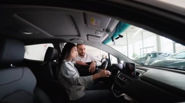 Araba satıcısı yeni araba almadan önce bayan bir müşteriye araba seçeneklerini gösteriyor. Kendine güvenen satıcı en iyi arabaları sunar.