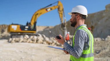 Foreman kazı makinesindeki işçilere taş ocağındaki telsizle talim talimatı veriyor. Taş ocağında taş çıkarma. Kum taşı madenciliği uzmanı. Açık maden endüstrisi kavramı