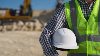 Elinde miğfer olan mühendis jeolog. Jeologun elindeki beyaz miğfer. Kazıcının yanındaki adam.