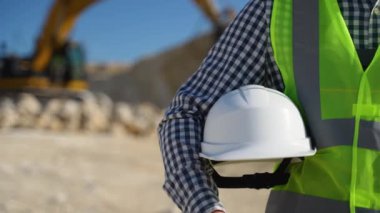 Elinde miğfer olan mühendis jeolog. Jeologun elindeki beyaz miğfer. Kazıcının yanındaki adam.