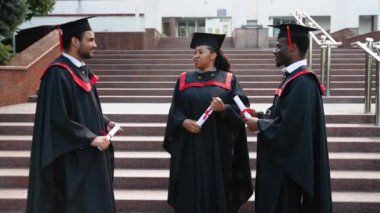 Üniversite kampüsünde konuşan çok ırklı mezunlar var. Diplomalarını kampüste tutuyor, mezuniyet günlerini kutluyor, yakın plan portre çekimleri yapıyor.