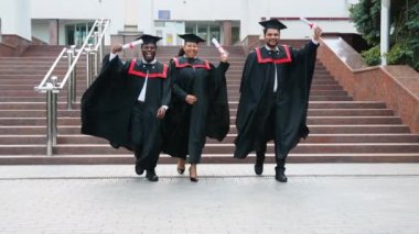 Çok ırklı çeşitli mezunlar mezuniyeti kutluyor, mezunlar kampüste koşuyor. Mezuniyet günün kutlu olsun.