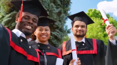 Mezuniyet elbisesi giymiş, özçekim yapan, gülümseyen ve mezuniyeti kutlayan üç farklı ırktan mutlu öğrenci. Mutlu anları yakalıyorum.