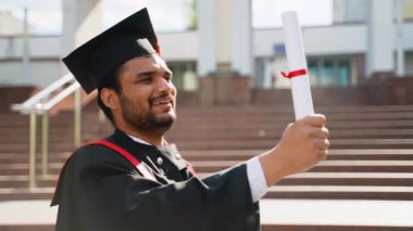Mezuniyet gününde üniversite kampüsünde diplomasıyla ayakta duran Hintli bir öğrenci. Eğitim, mezuniyet ve halk konsepti - Manto ve şapka giymiş Hintli Asyalı öğrenci