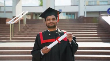 Üniversite yakınlarında diplomalı Pakistanlı bir öğrencinin portresi. Eğitim, mezuniyet ve halk konsepti - Manto ve şapka giymiş Hintli Asyalı öğrenci