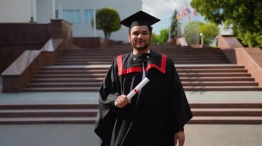 Manto mezunu Hintli bir öğrenci üniversite kampüsünde yürüyor ve mezuniyeti kutluyor. Eğitim, mezuniyet ve halk konsepti - Manto ve şapka giymiş Hintli Asyalı öğrenci