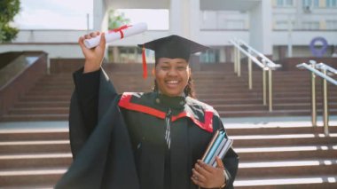 Afrikalı Amerikalı kız öğrenci üniversitenin yakınındaki mezuniyeti kutluyor. Eğitim, mezuniyet ve halk konsepti - Afrika kökenli Amerikalı kız öğrenci manto ve şapka açık havada