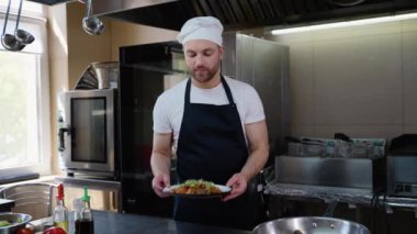 Gülümseyen aşçı restoran mutfağında Asya yemeği tabağı tutuyor. Yemek pişirme, meslek ve insan konsepti. Otel mutfağında profesyonel aşçı.