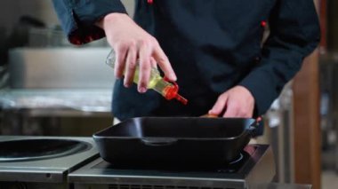 Şef tavaya ayçiçeği ya da zeytinyağı döker, yakın çekim. Pişirmeye hazır et tavası.