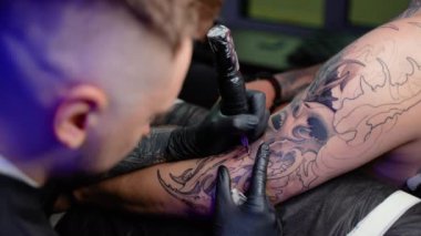Dövme salonu. Dövme ustası bir erkeğin eline dövme yaptırıyor. Dövme makinesi, güvenlik ve hijyen. Yakın plan, renkli, dövmeci.