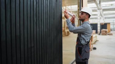 Prefabrik eve pencere kurarken köpük kullanan işçiler. Bileşik ahşap panellerden yeni ve modern prefabrik modüler evler inşa ediliyor. Enerji verimli panel montajı