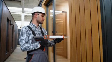 Bir işçi prefabrik modüler evdeki kuşak ve pencere çerçevesi arasındaki boşluğu doldurmak için poliüretan köpük uyguluyor. Bileşik ahşap panellerden yeni ve modern prefabrik modüler ev inşaatı